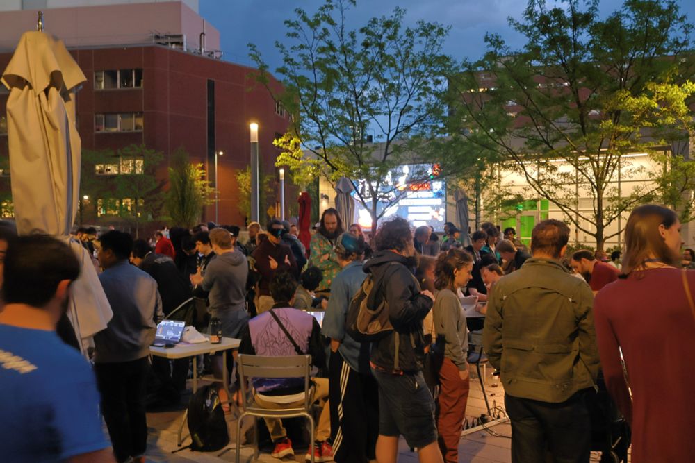 The Boston Indies Demo Night. A crowd of game devs socializing and playing demos outdoors in the evening.