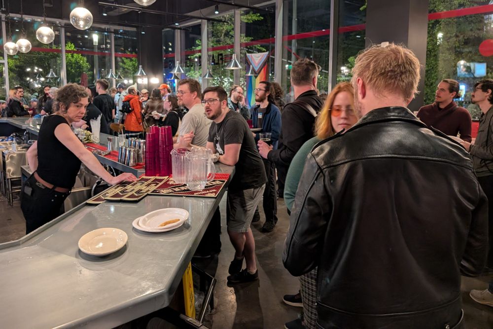 Our Make Games Make Friends event. A crowd gathered indoors is chatting and ordering drinks.