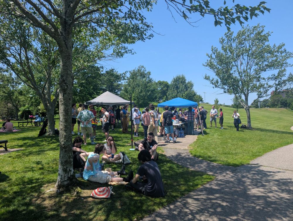 People sitting on the grass and gathering under tents in the park.