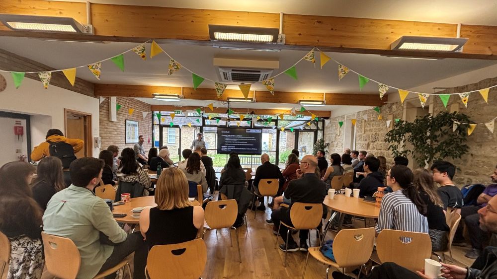 A room full of people watching a man present at the front.