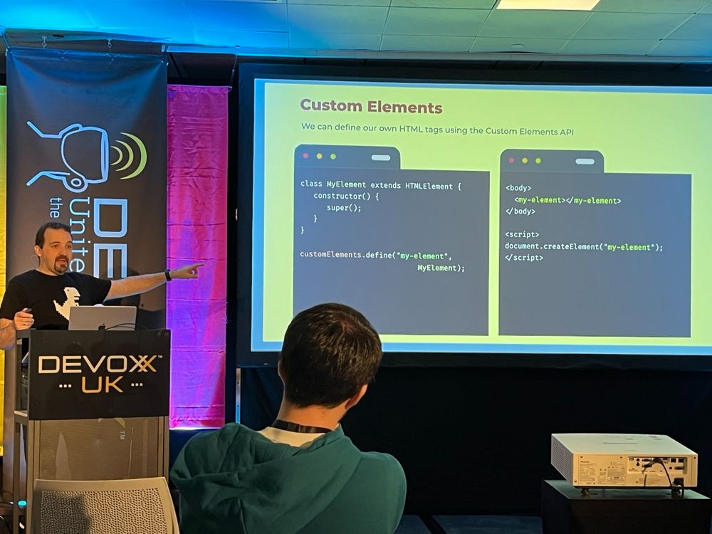 Max pointing to slide showing example code for Custom Elements

(Left side of slide):

class MyElement extends HTMLElement {
constructor() {
super();
customelements. define ("my-element",
MyElement);

(Right side of slide:)

‹body>
</body>
‹my-element></my-element>
< script>
document.createElement ("my-element*);
‹/script>
