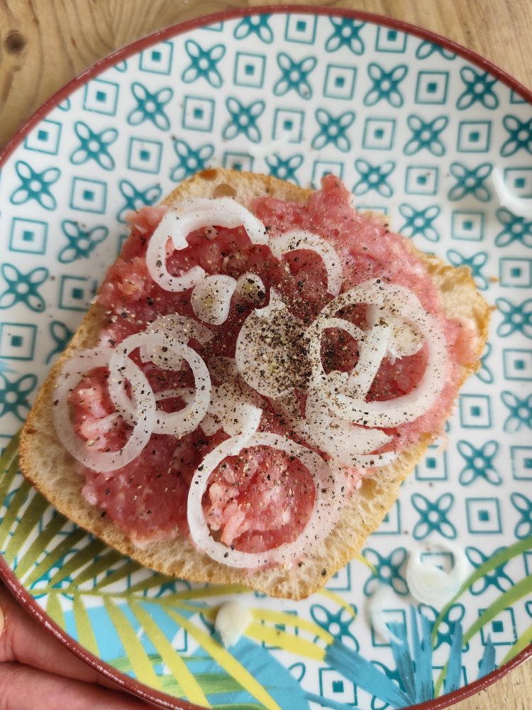 Foto da metade de um pão francês com carne moída, cebola e pimenta do Reino.
