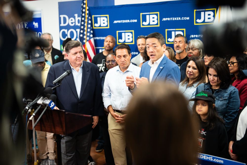 House Majority Leader Gene Wu speaks at a press conference. Several legislators, and Illinois Governor JB Pritzker, stand behind him.