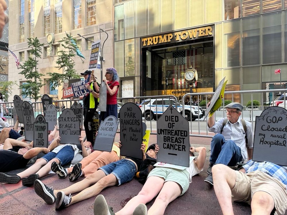 People laying down in front of Trump Tower holding cardboard tombstones 