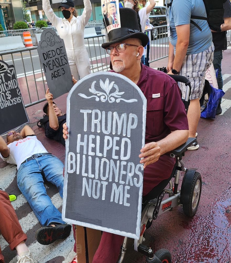 A person holding a cardboard tombstone that says “Trump helped billionaires not me”