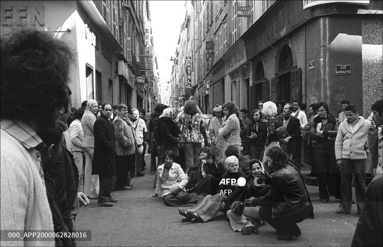 Groupe de femmes assises et debout dans la rue, quelques hommes parmi elles. Une cinquantaine de personnes en tout.