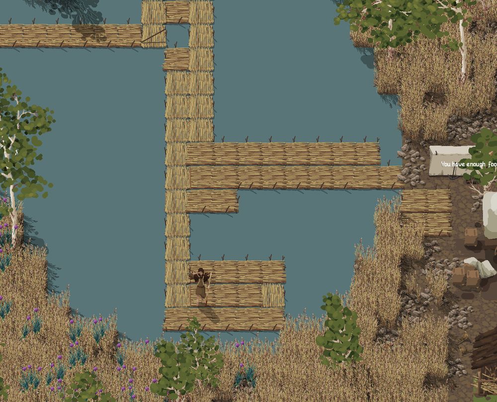 A pixel art researcher stands on a reeds pontoon within a small lake. A small platform has been created around them with a path going up and then to the right to reach land and a second path going up and then to the left off the screen. On the right you can spot some buildings, though none of them are entirely within the picture. Around the lake rocks and reeds can be found. Occasionally a riverbirch tree sticks out from in-between the tall reeds. 