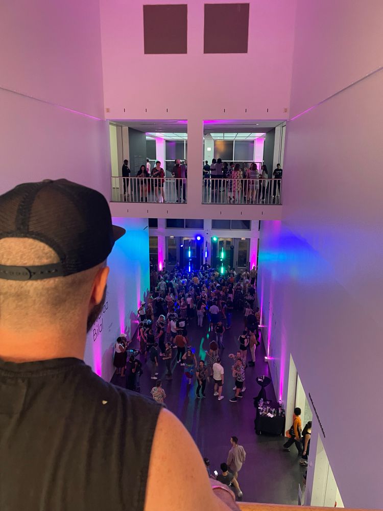 A photo of the art gallery floor from the upstairs balcony over a man’s shoulder 