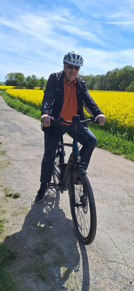 Ralf Sandfuchs auf dem E-Bike vor einem blühenden Rapsfeld