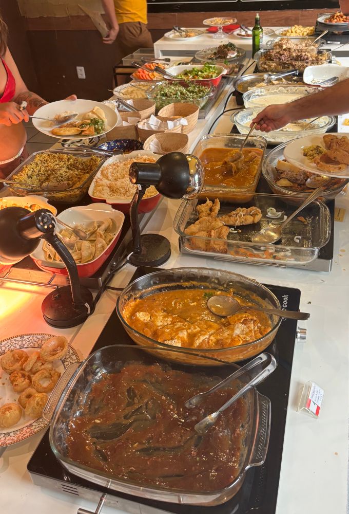 mesa de um buffet do festival árabe. os pratos são: esfihas variadas, sambousek, shawarma de carne e frango, talamezaatar, pão folha e acompanhamentos (homus, coalhada seca, pasta de alho), tabule, fatouche, saladas (tomate, pepino e alface), kibe frito, kibe armeno, kibe cru, falafel, kafta, charutinho de repolho, arroz de cordeiro, miadra, arroz com aletria, mousaka, chichibarak, kibe labanie, shakshuka (ovos com molho de tomate) e peixe empanado com molho tahine.