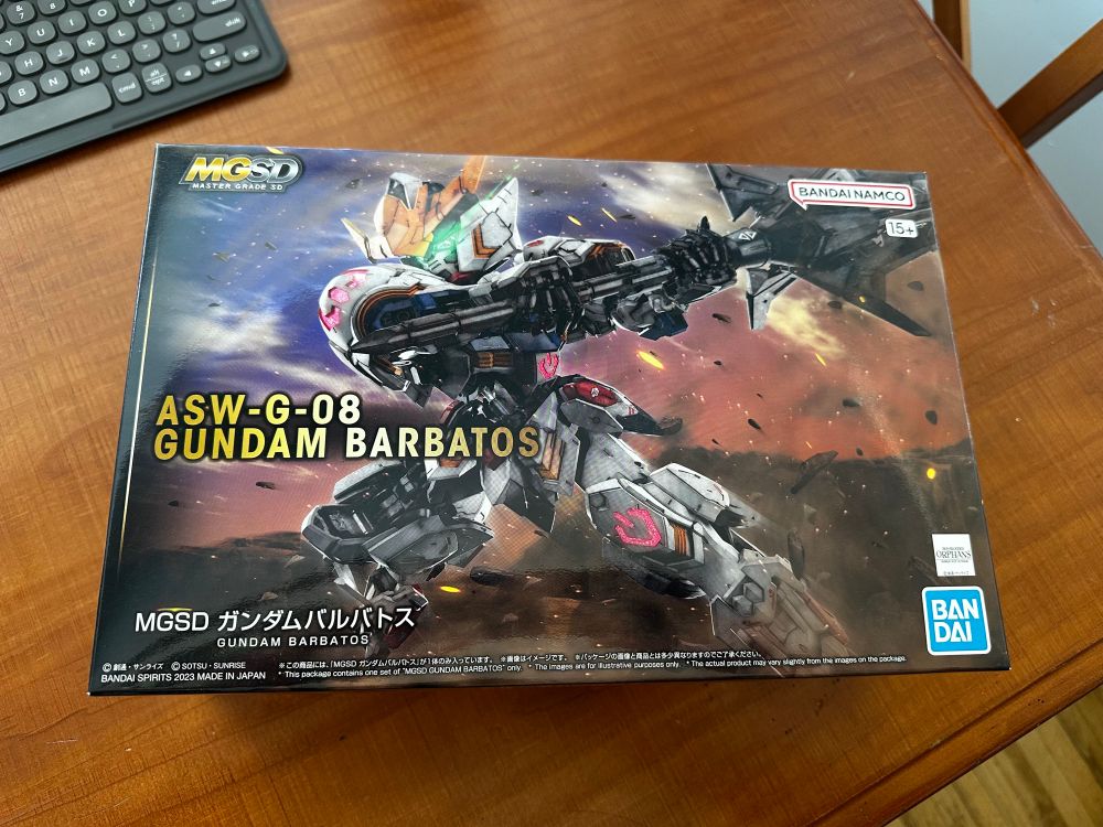 Top box art for the MGSD Barbatos. Box is sitting on a wood table. 