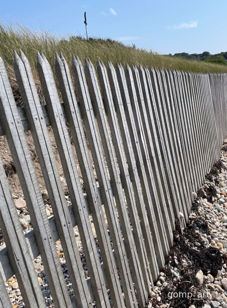 Wooden fencing stretching across a rocky beach. gomp_art