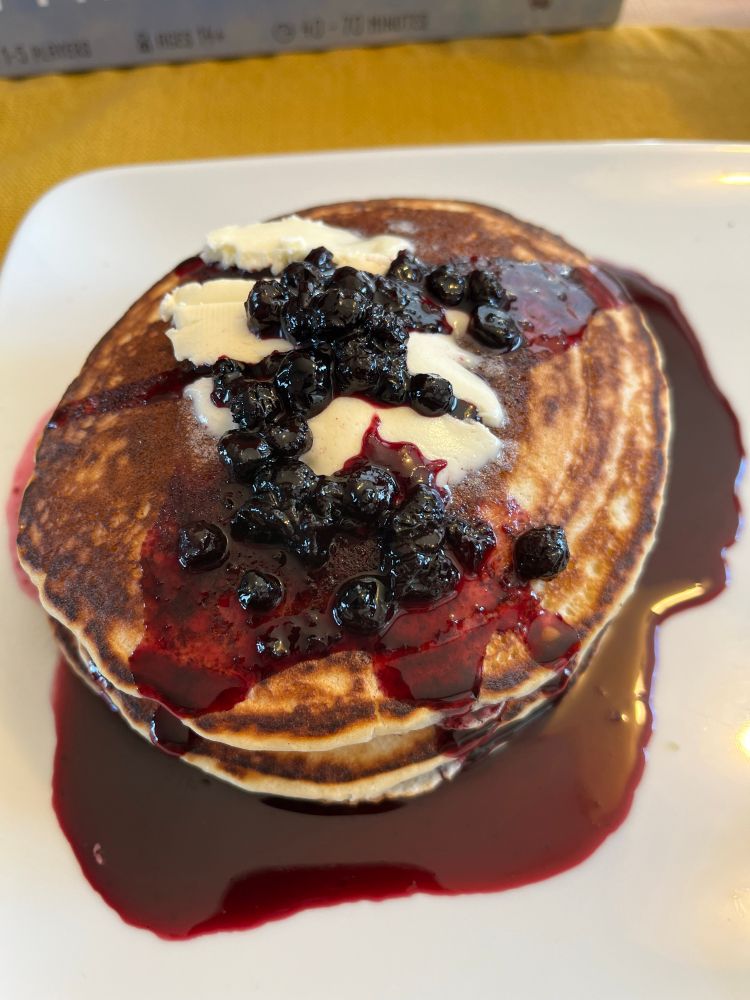 A stack of pancakes covered in butter and blueberry syrup.