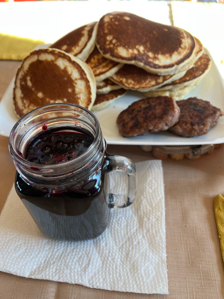 A big plate of pancakes and sausage patties next to a jar of homemade blueberry syrup.