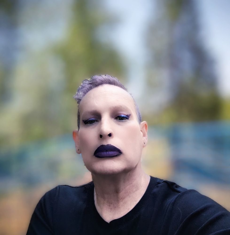 white woman in black top with short purple hair and black and purple makeup 