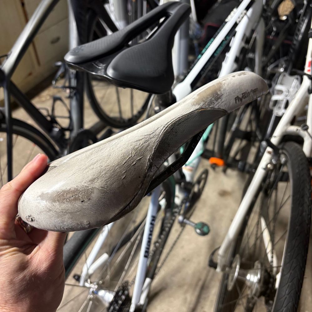 An old, worn, whitebike saddle showing a lot of wear in front of several bicycles. 