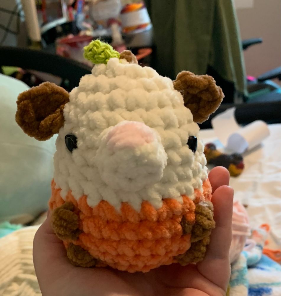 A white brown and orange possom with a small stem and leaf on its head, front view 