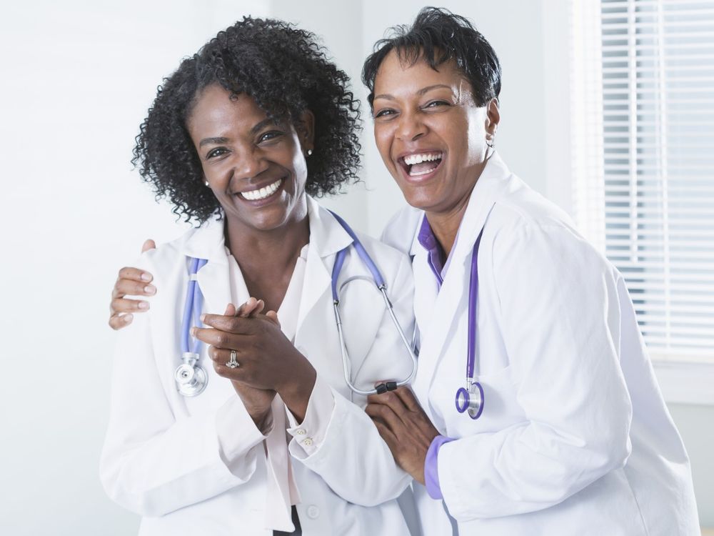 Two medical professionals in lab coats smiling and standing close together in a friendly pose.