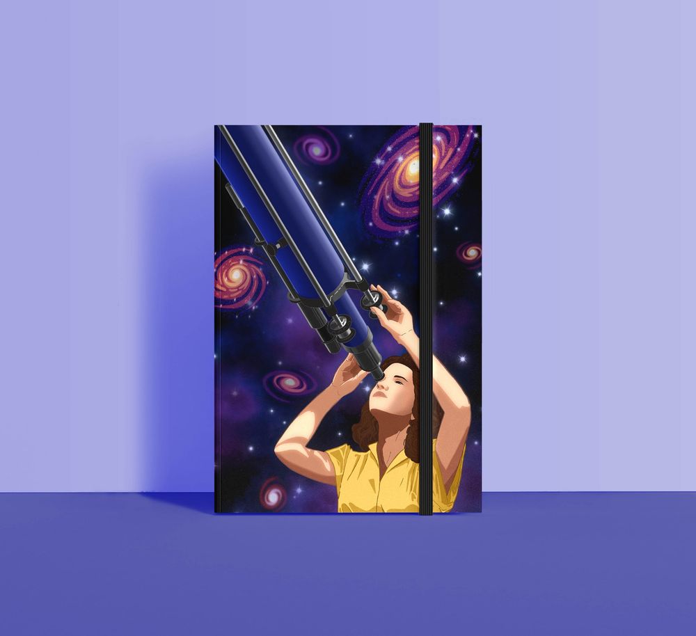 caderno com ilustração de uma mulher usando um telescópio azul. No fundo, várias galaxias espirais coloridas e estrelas brilhantes. O caderno tem um elastico preto pra segurar a capa.