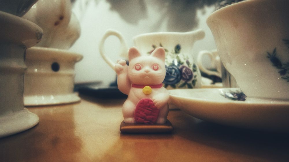 A tiny lucky cat figurine on a table of teacups. 