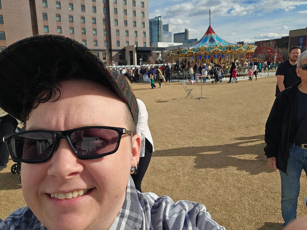 Kalen stands with a carousel behind them in downtown Denver on Auraria Campus.