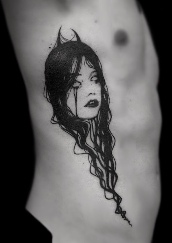 Photo of a tattoo on man’s ribs, black background. Dark portrait tattoo of a lady with devil horns, hollow eyes, tears and long flowy black hair all around. 