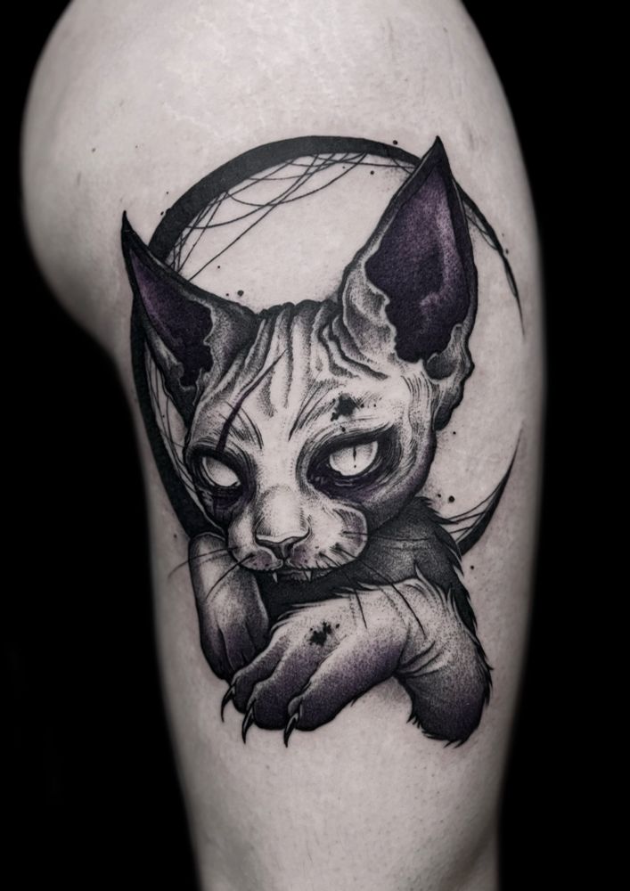 Big black and purple tattoo on a thigh of an undead vampire Devon Rex cat. Crescent black moon in the background. 