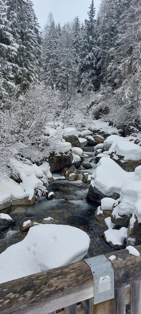 Eine verschneite Winterlandschaft mit einem Bach, fotografiert von der Brücke aus.