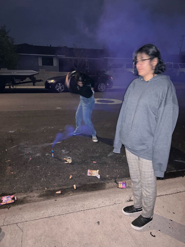 One person standing straight as another in the background in swinging hunched over a stream of smoke 