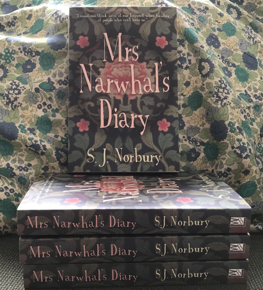 Pile of paperbacks of Mrs Narwhal's Diary by SJ Norbury, spines out. One copy sitting on top face out. Background is a green, blue and yellow floral cushion. 