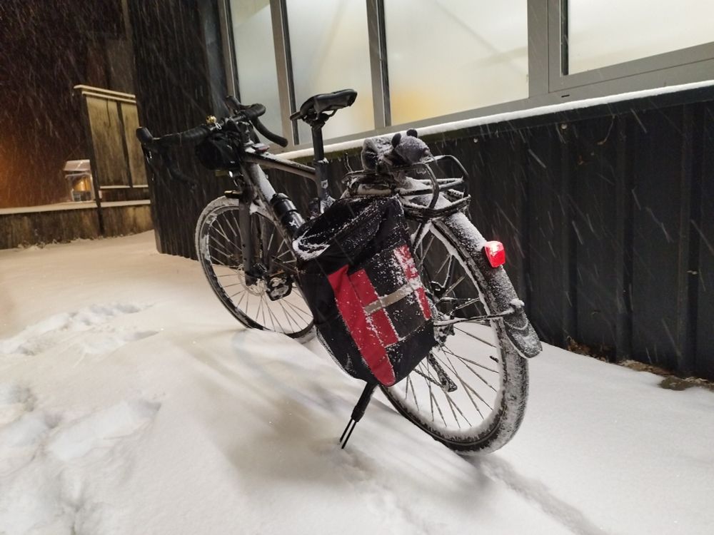 Ein Gravelbike eingeschneit im Schnee. Links an der Seite ist eine rote Tasche montiert.