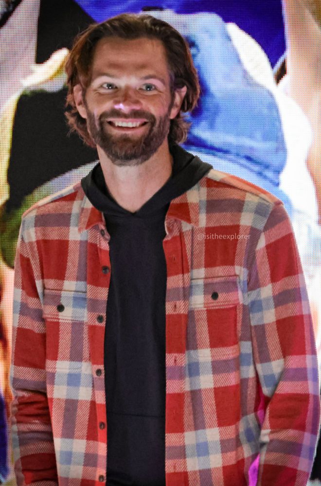 Photo of Jared, wearing a black hoodie + red plaid . He's smiling at the audience