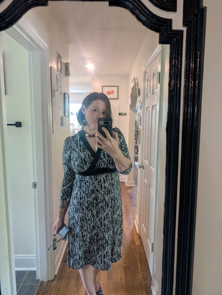 Mirror selfie of a white woman in black heels, a black and white patterned dress and nicely done makeup and coiffed hair