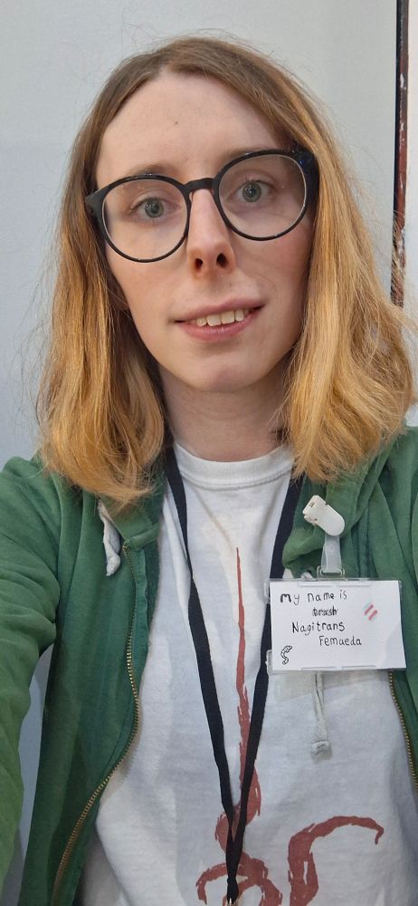 A selfie of a lady dressed like Nagito from Danganronpa, wearing a name badge that says "my name is Nagitrans Femaeda". The word "trash" is scribbled out.