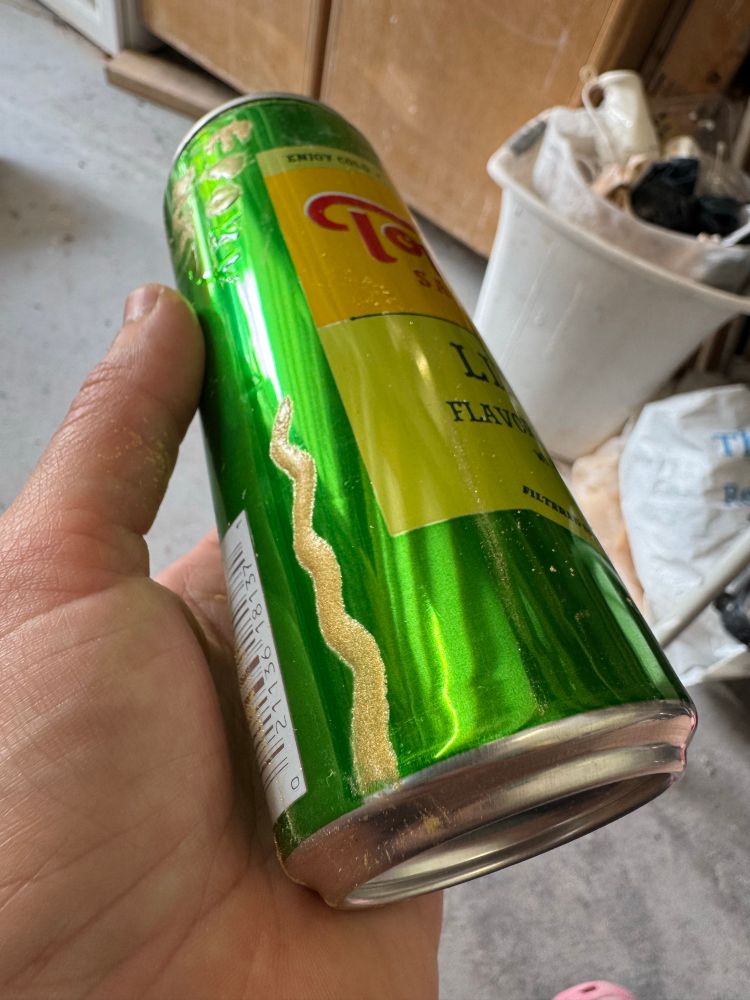 A topo Chico can with a plump golden line on it. I like the roundness of the golden line, but the powdered mica that gives it the color is too dull. 