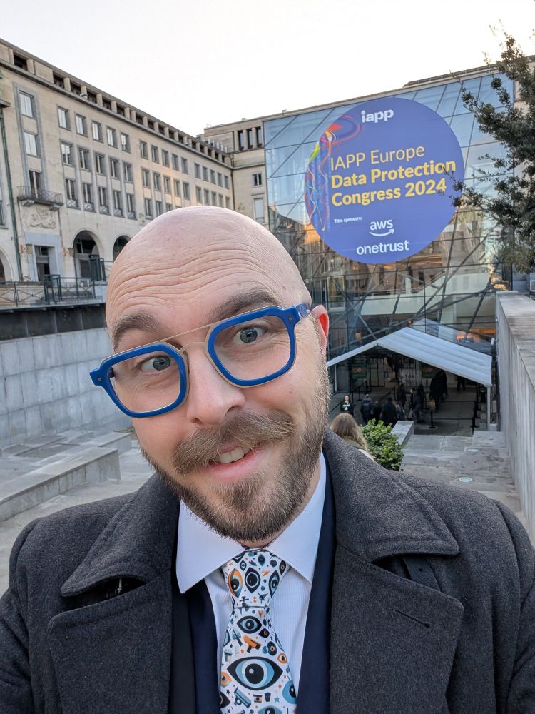 Cobun stands in front of the Brussels conference venue in a winter jacket and wearing a tie with a print of eyeballs and other surveillance themes. 