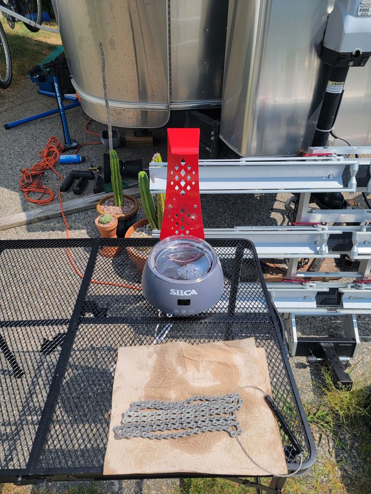 In the foreground, a just de-greased bike chain and a Silca wax pot. in the background, a receiver mounted bike rack, 3 pots of cacti and an Airstream trailer.