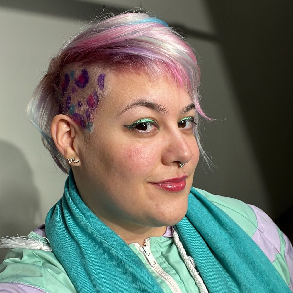 Eu sorrindo com meu cabelo platinado com mechas rosa, roxa e azul e a lateral raspada com oncinha colorida. Estou usando um delineador cromado verde e azul e um protetor labial rosado