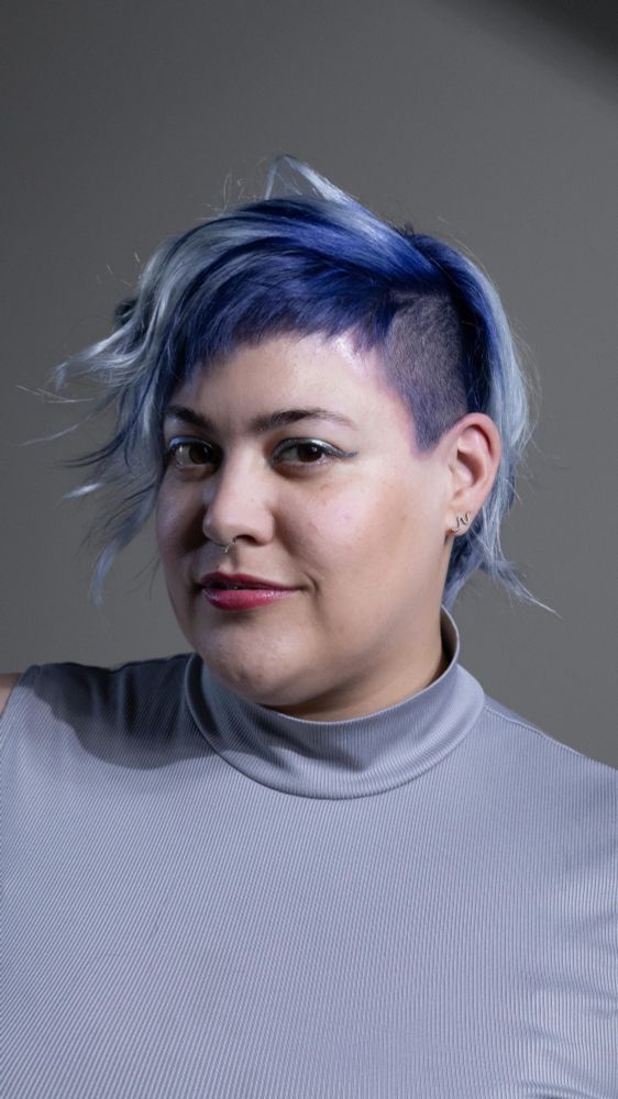 Mesma configuração de foto editorial mas dessa vez meu rosto está virado pro outro lado mostrando a lateral raspada e pintada de azul do meu cabelo, dou um leve sorriso