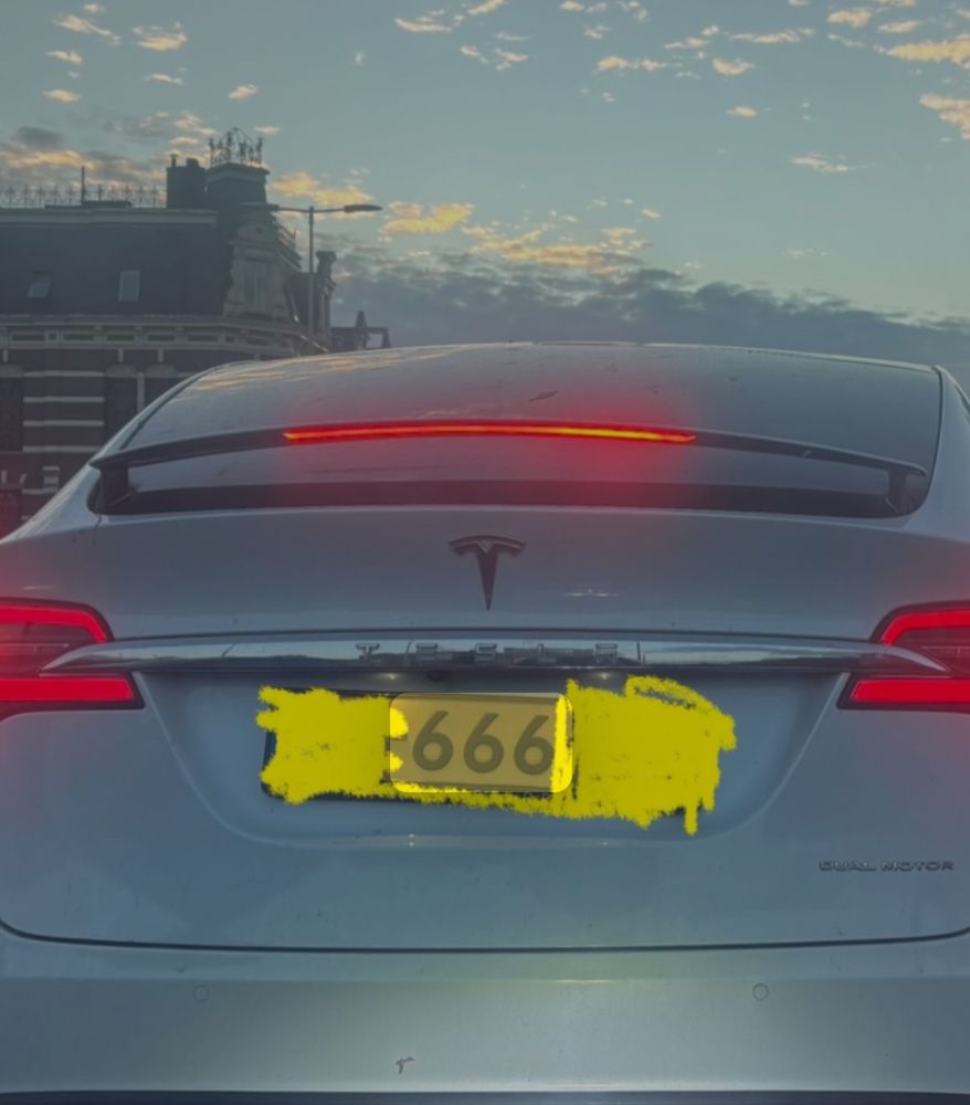 Witte Tesla Van de achterkant gefotografeerd, bij schemer, achterlicht en remlicht aan, nummerbord voor een gedeelte onleesbaar gemaakt behalve het getal 666
