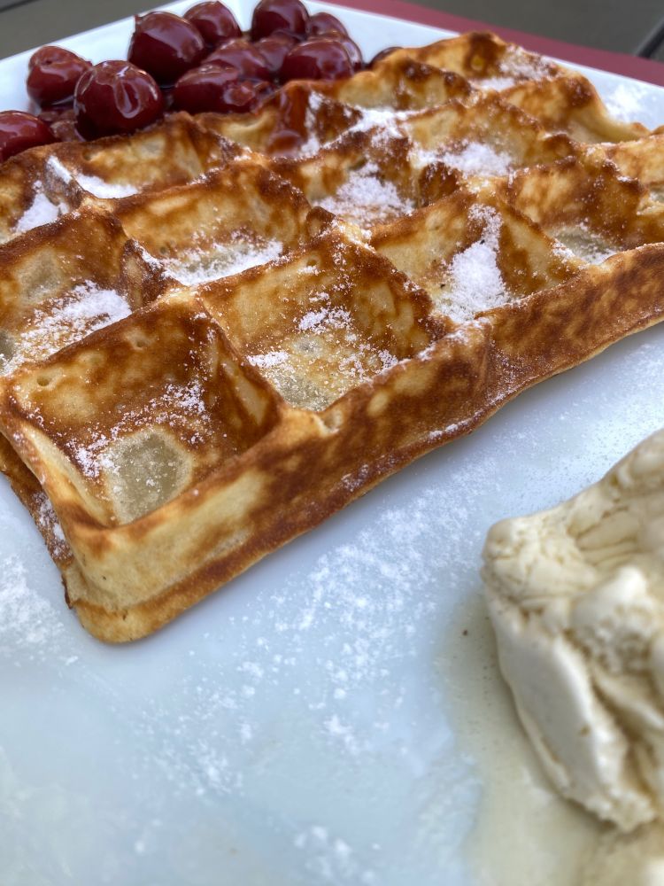 A waffle with hot cherries and vanilla ice cream.