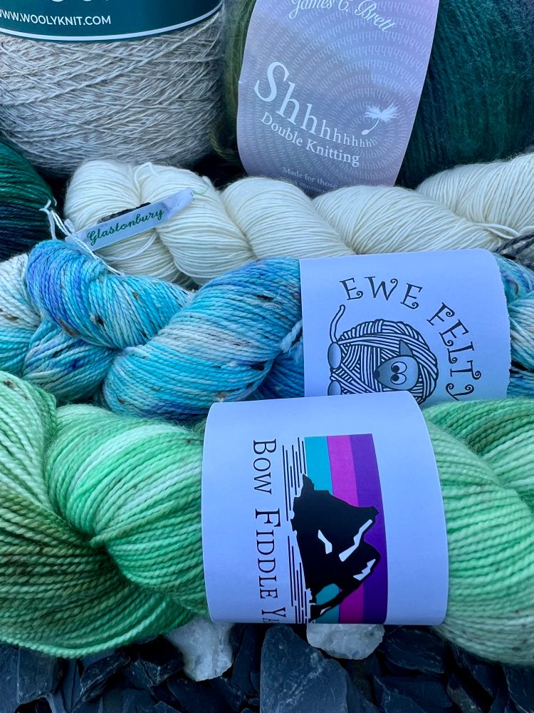 A closeup view of three skeins of yarn. They are hand dyed green, blues, and an undyed single ply handspun. 