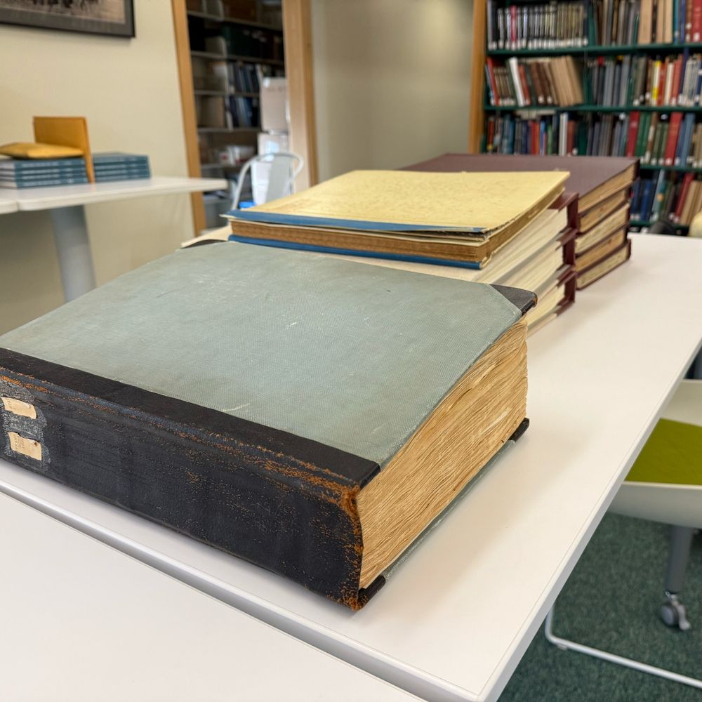 A series of large scrapbook volumes sit on a table in a library. The closest album is the oldest and the fattest. 
