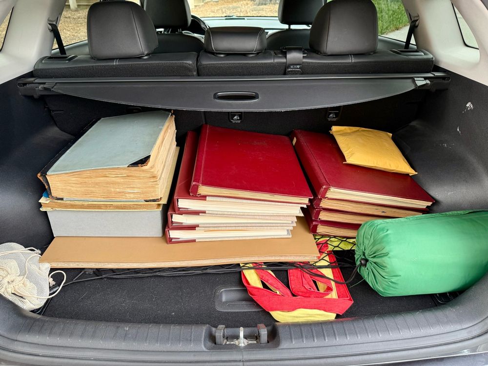 The trunk of a small SUV has several large books and albums stacked in the back. 