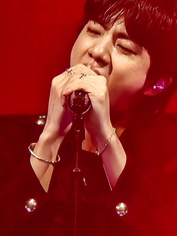 Jin wearing black but the aura is red, holding his mic while singing. 