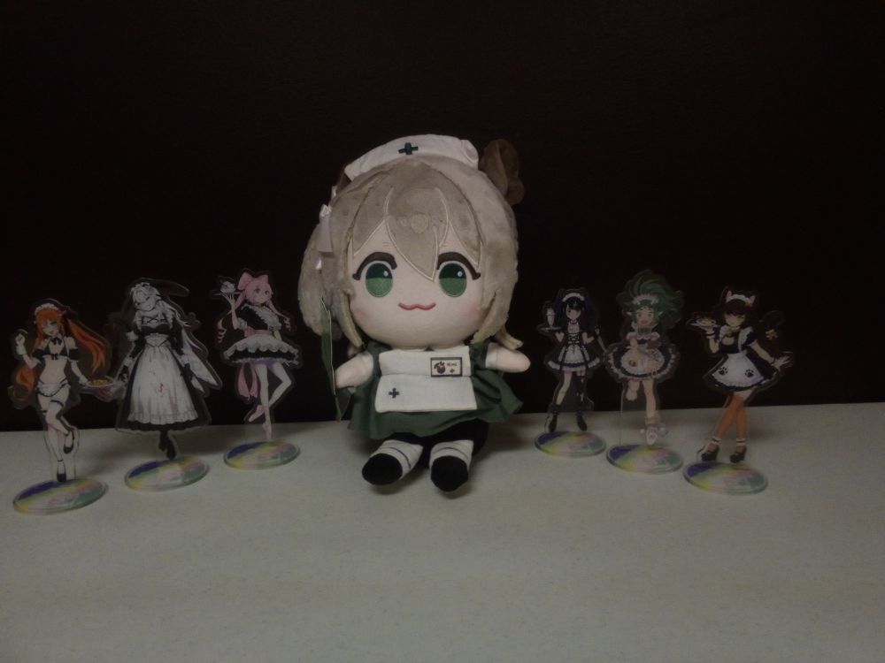 A Nimi Nightmare plushie in the midst of standees of the ladies of 3AM dressed as maids.  Those ladies being Fang Guu, Lyra Calyptra, Olivia Monroe, Coqui Saporana, Meat S. Cave, and Callie Calico.
