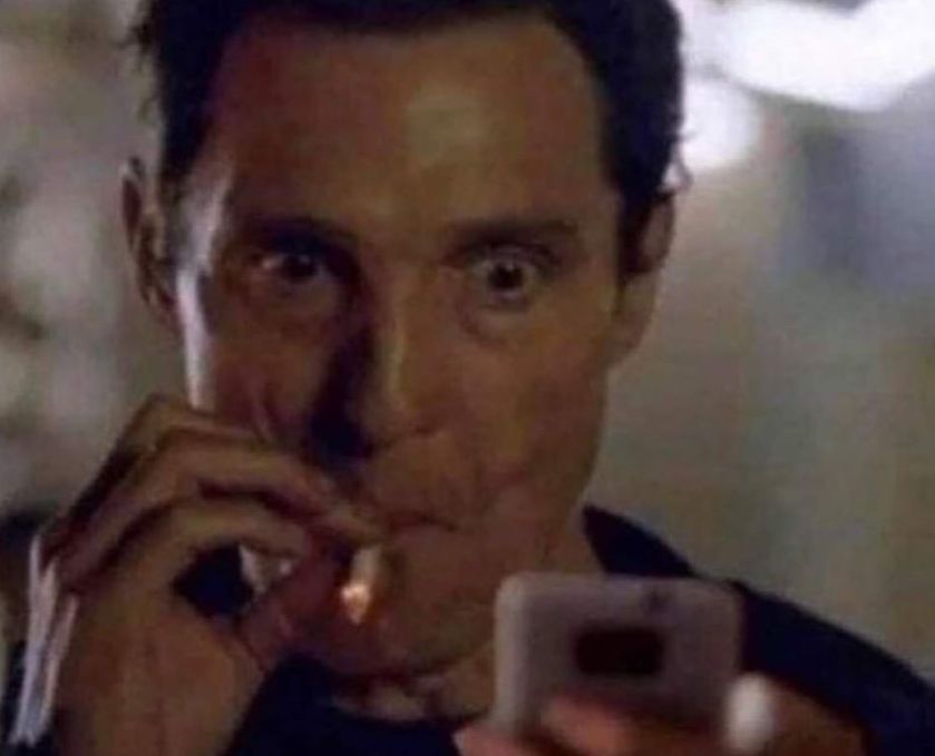 Matthew McConaughey dragging on a cigarette looking at his phone 