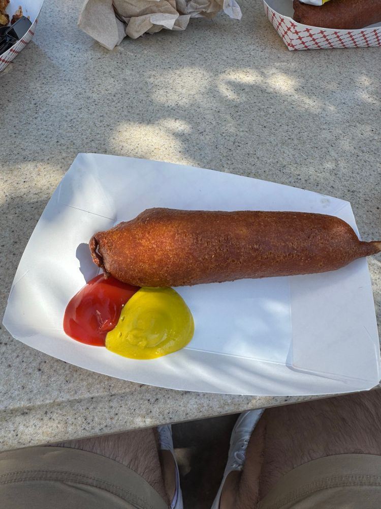 A corn dog with a funny looking tip next to some ketchup and mustard 