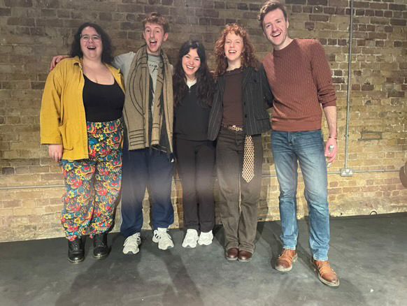Four smiley happy artists are laughing for the photographer against a brick wall 