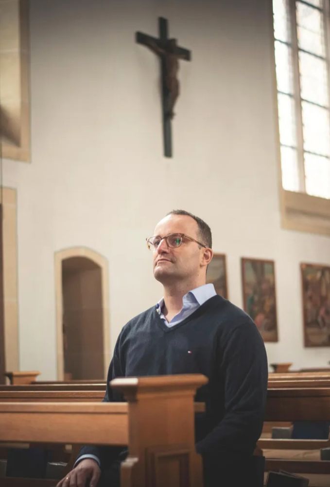 Bild von Jens Spahn in einer Kirche, während er auf einer Kirchbank ist, über ihm an der Wand ein Kruzifix.